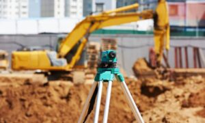 Topographic survey equipment set up on a Boston construction site with excavators in the background