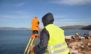 Surveyor conducting an elevation survey near a coastal property after storm waves
