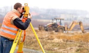 Licensed land surveyor on construction site - ALTA SURVEY Massachusetts Licensed land surveyor conducting a construction survey with a total station at an active construction site