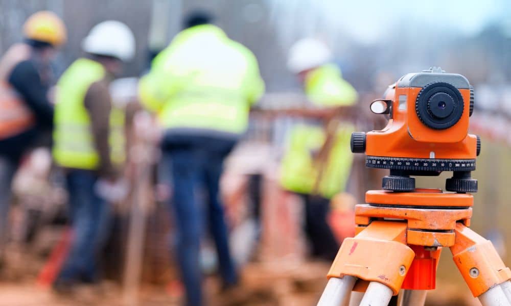 Construction surveyors using surveying equipment on a construction site, with workers in safety gear
