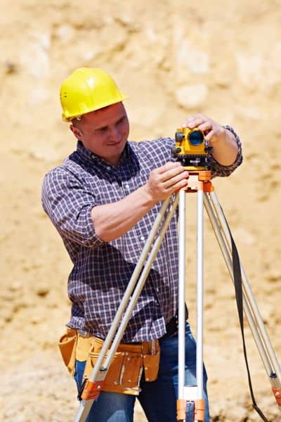 Land surveyor using leveling equipment to measure elevation changes during a topographic survey