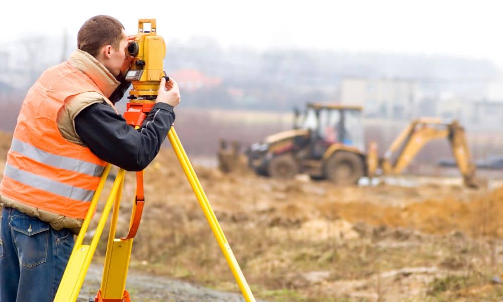 Licensed land surveyor on construction site - ALTA SURVEY Massachusetts Licensed land surveyor conducting a construction survey with a total station at an active construction site