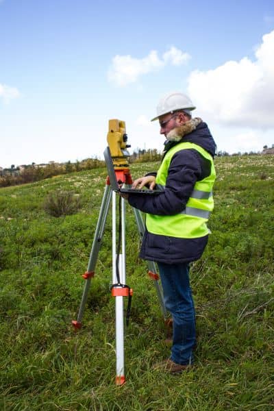 Surveyor using equipment to measure land elevation and boundaries for accurate property assessment